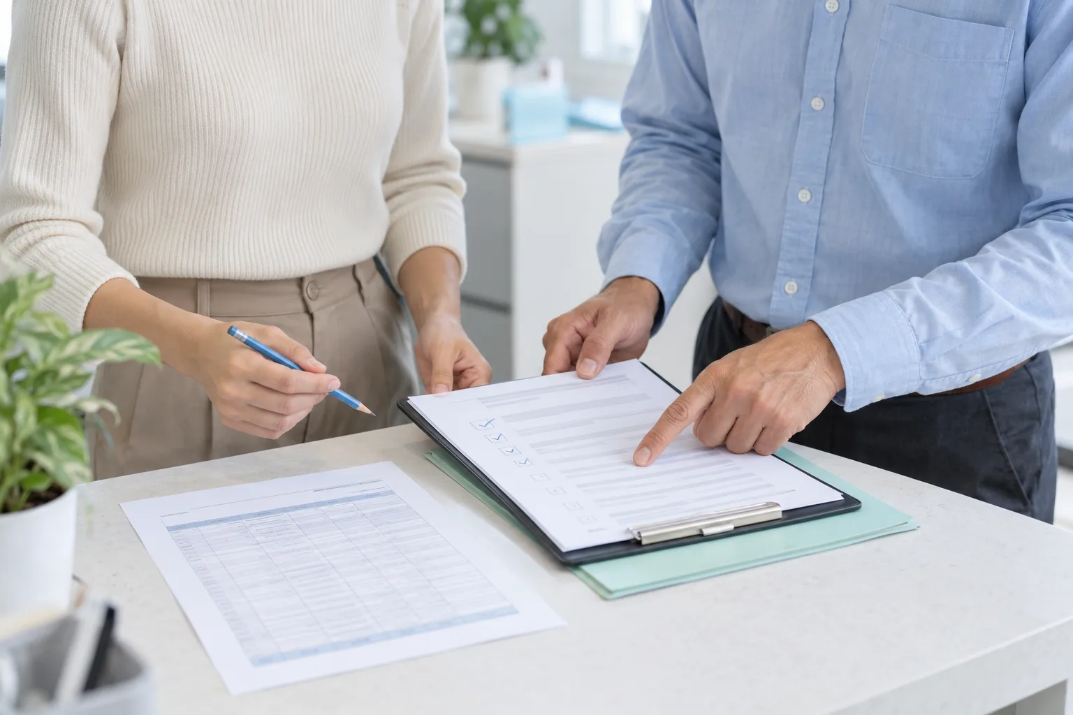 Two people compare a clipboard checklist with a separate time-record sheet at an office counter.